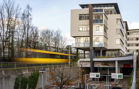 Ein- und Ausfahrt zum Park + Ride Parkhaus an der Albstraße in Stuttgart Degerloch mit dem darüberstehenden Gebäude sowie einer vorbeifahrenden SSB Stadtbahn.