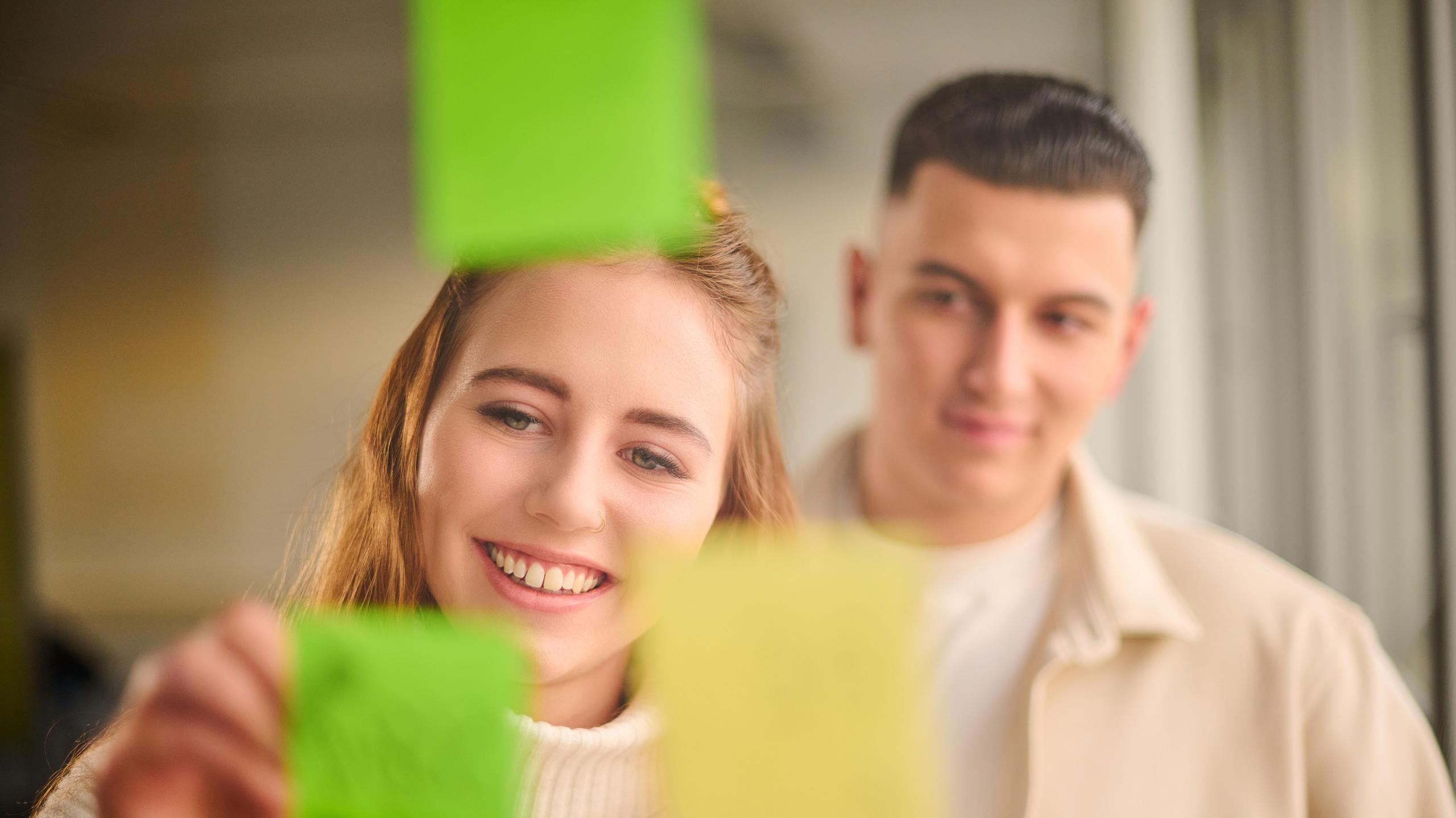 Eine junge Frau und ein junger Mann beschriften Post-it-Zettel.