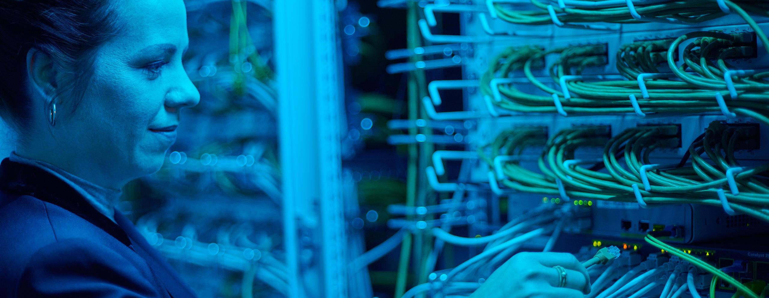 Eine IT-Mitarbeiterin steckt ein Netzwerkkabel ein.