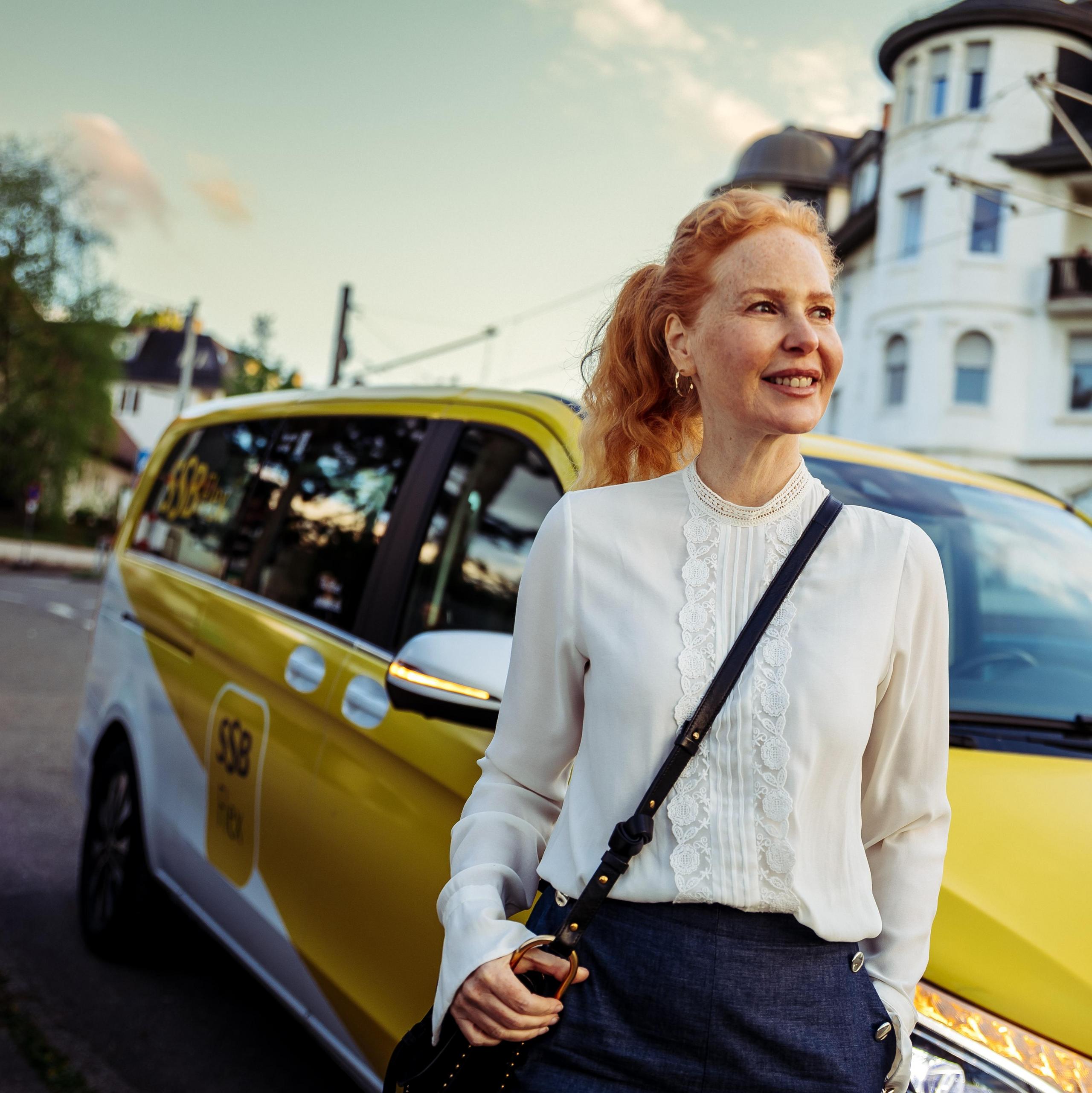 Frau mittleren Alters, die vor einem SSB Flex- Fahrzeug steht.