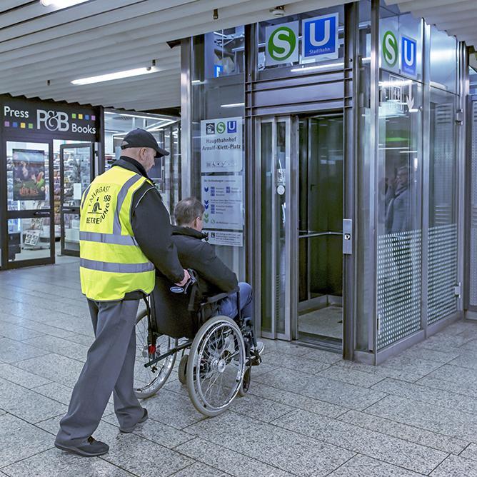Fahrgastbetreuer hilft Rollstuhlfahrer in einen Aufzug