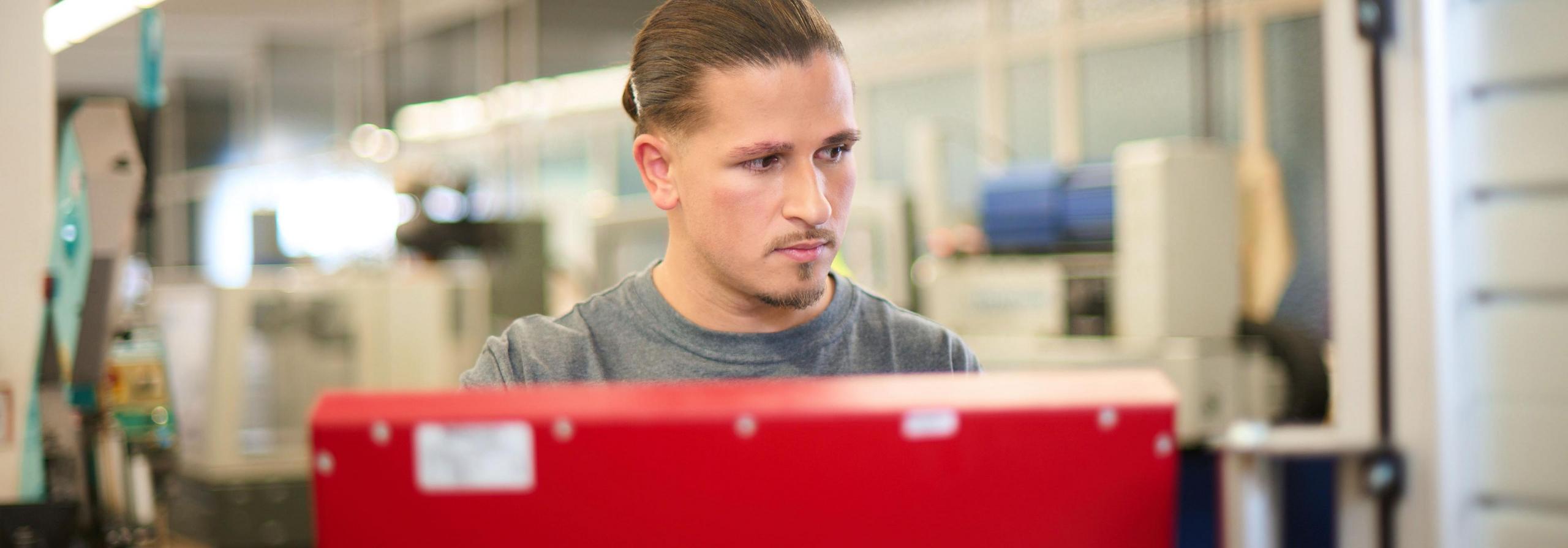 Ein Werkstudent steht vor einer Maschine.