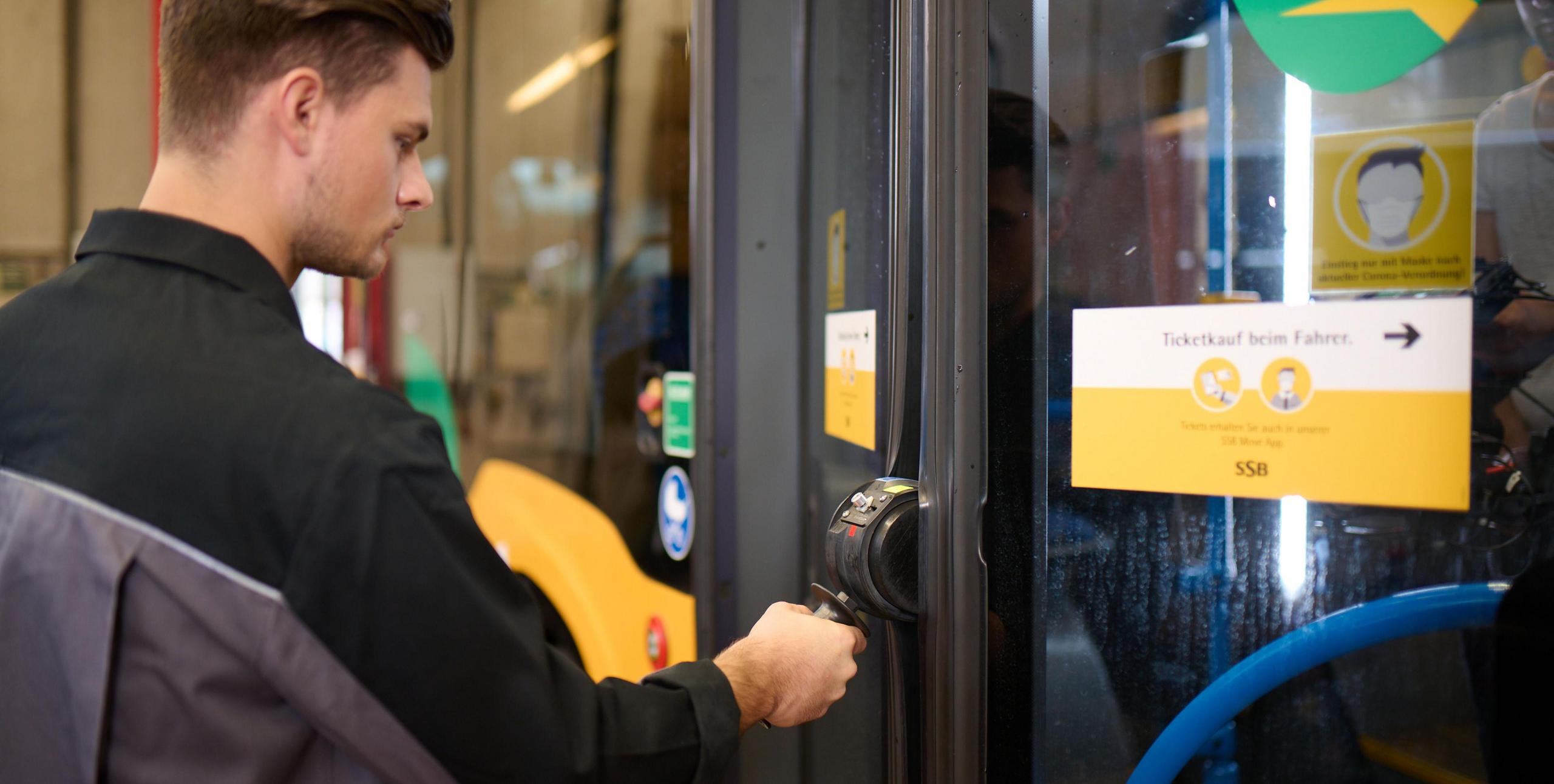 Ein Auszubildender in Werkstattkleidung prüft eine Bustür.