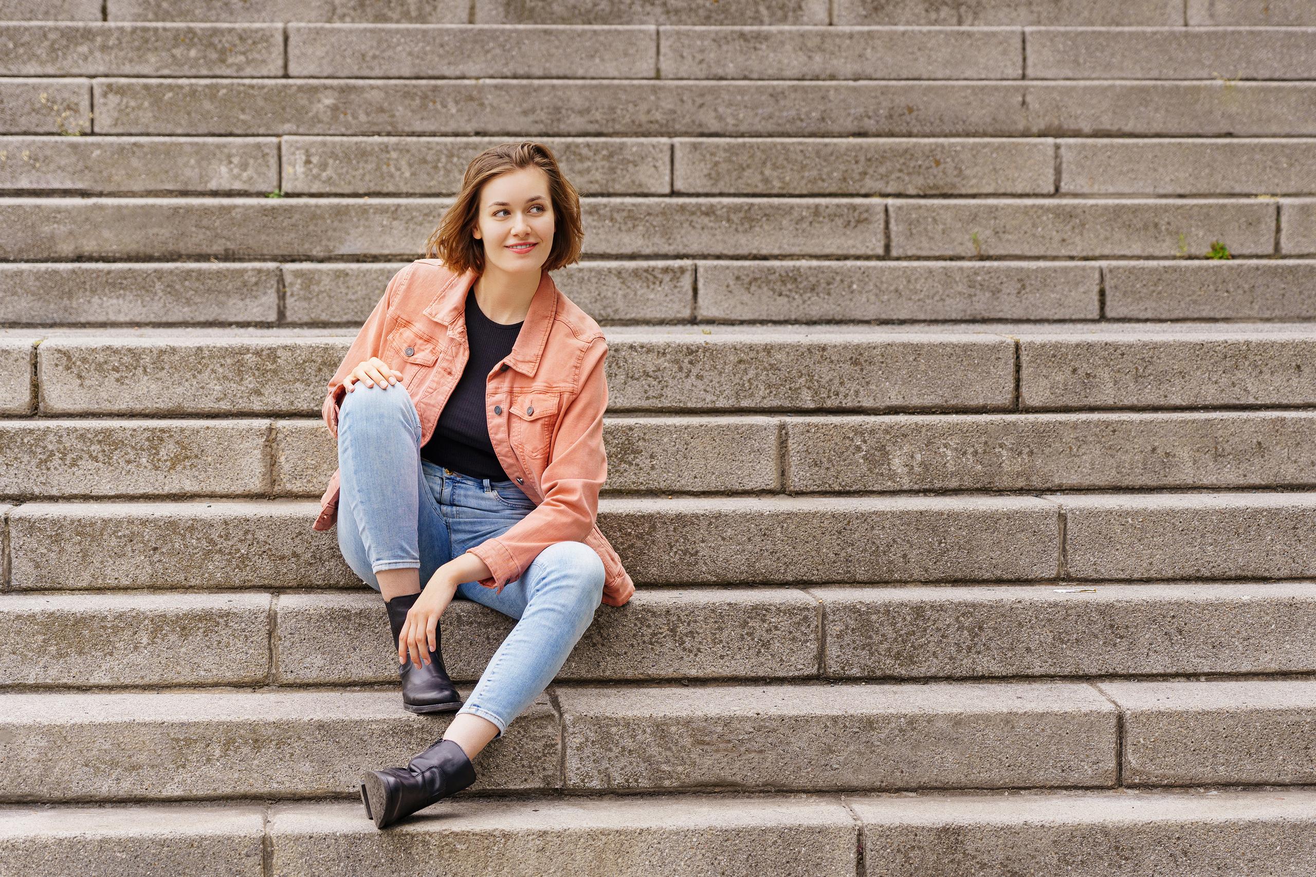 Eine junge Frau sitzt lächelnd auf einer großen Treppe.