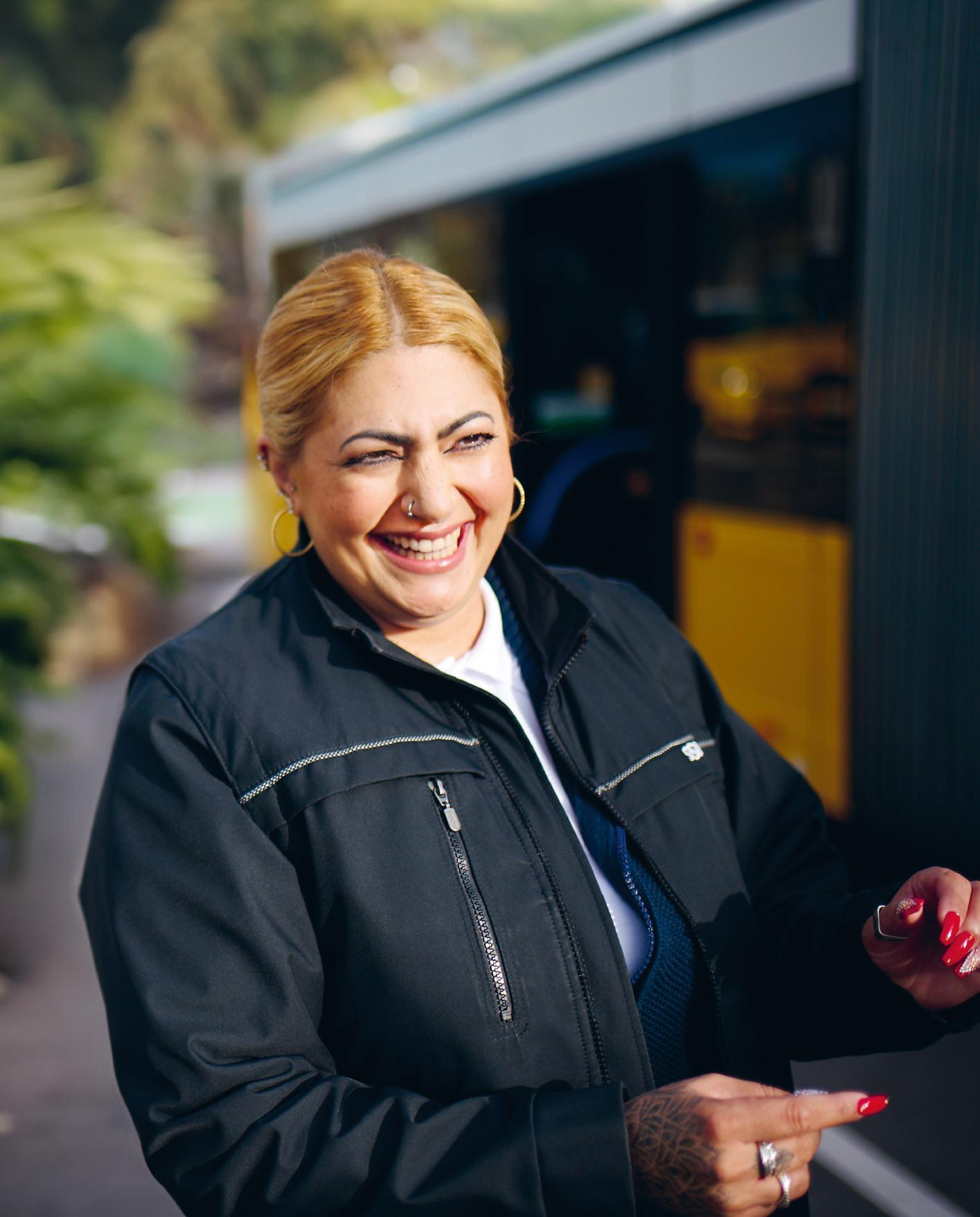 Eine Busfahrerin steht neben einem Bus und lächelt.