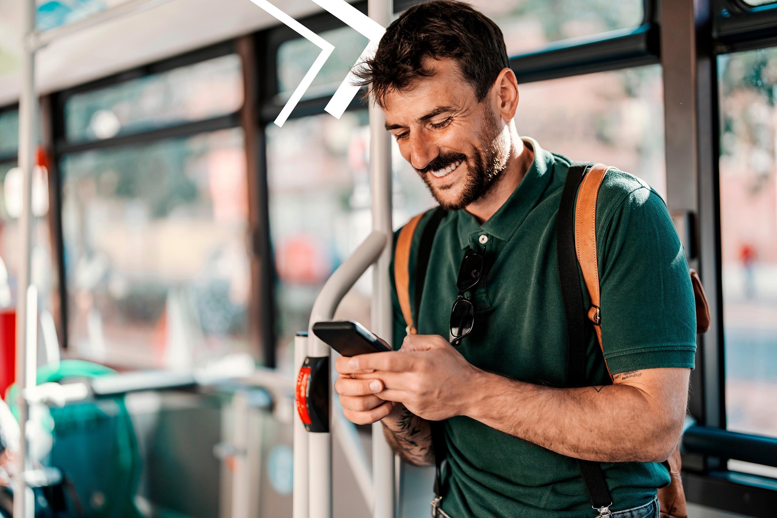 Ein im Bus stehender Mann schaut lächelnd auf sein Smartphone.