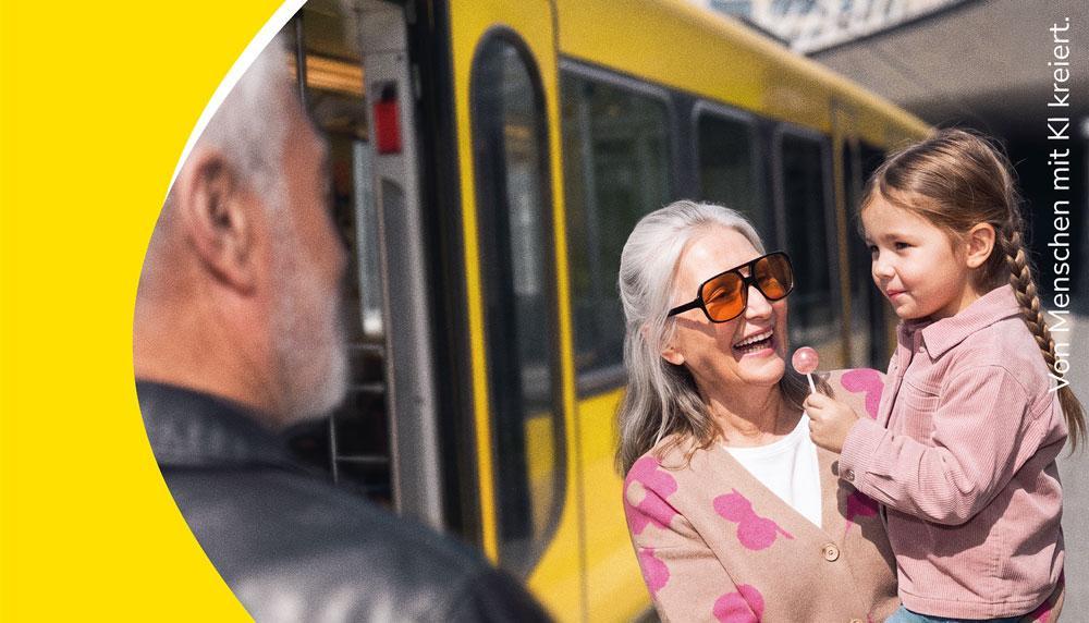 Ein ältere Dame steht neben einer Stadtbahn, trägt ein kleines Mädchen im Arm und lächelt.