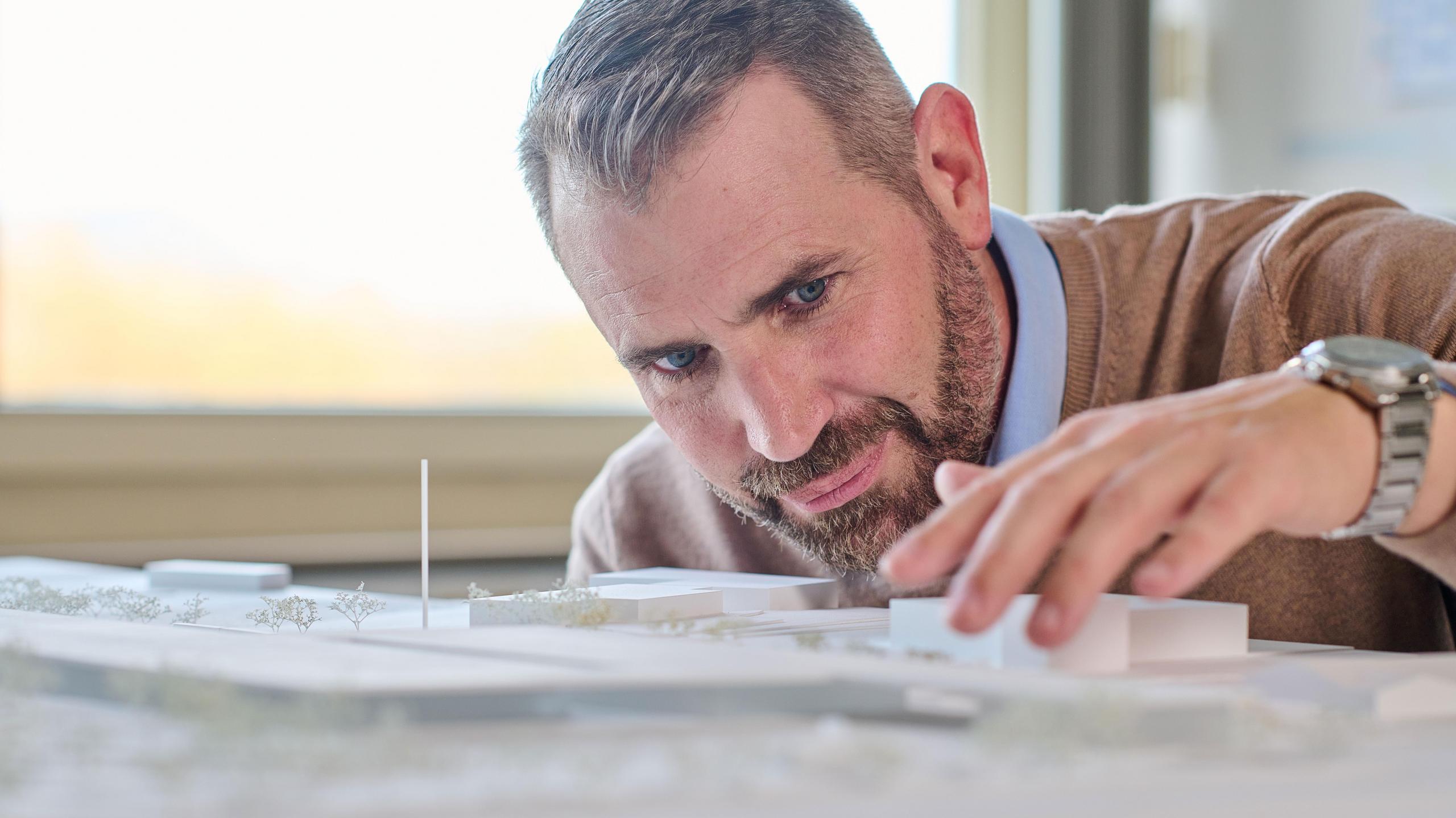 Ein Mann mittleren Alters schaut sich ein Gebäudemodell aus der Nähe an.