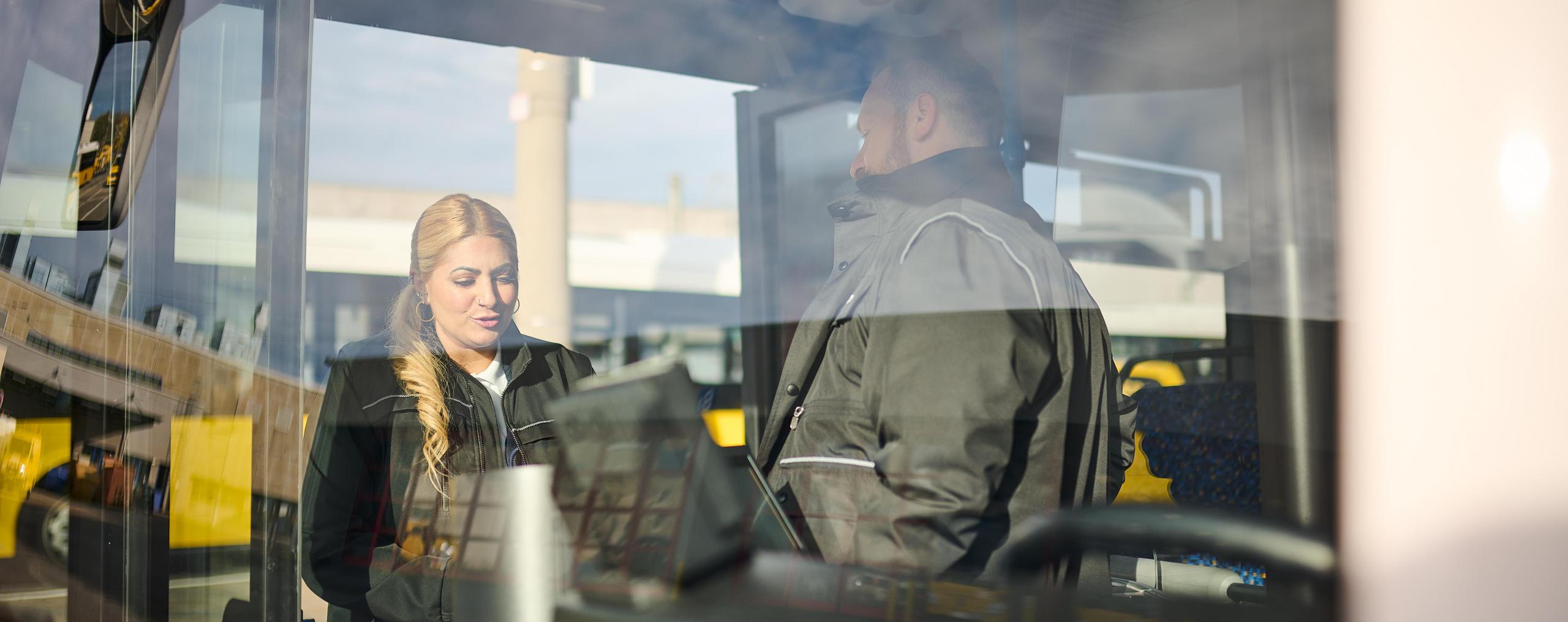 Eine Busfahrerin und ein Busfahrer unterhalten sich im Eingangsbereich eines Busses.