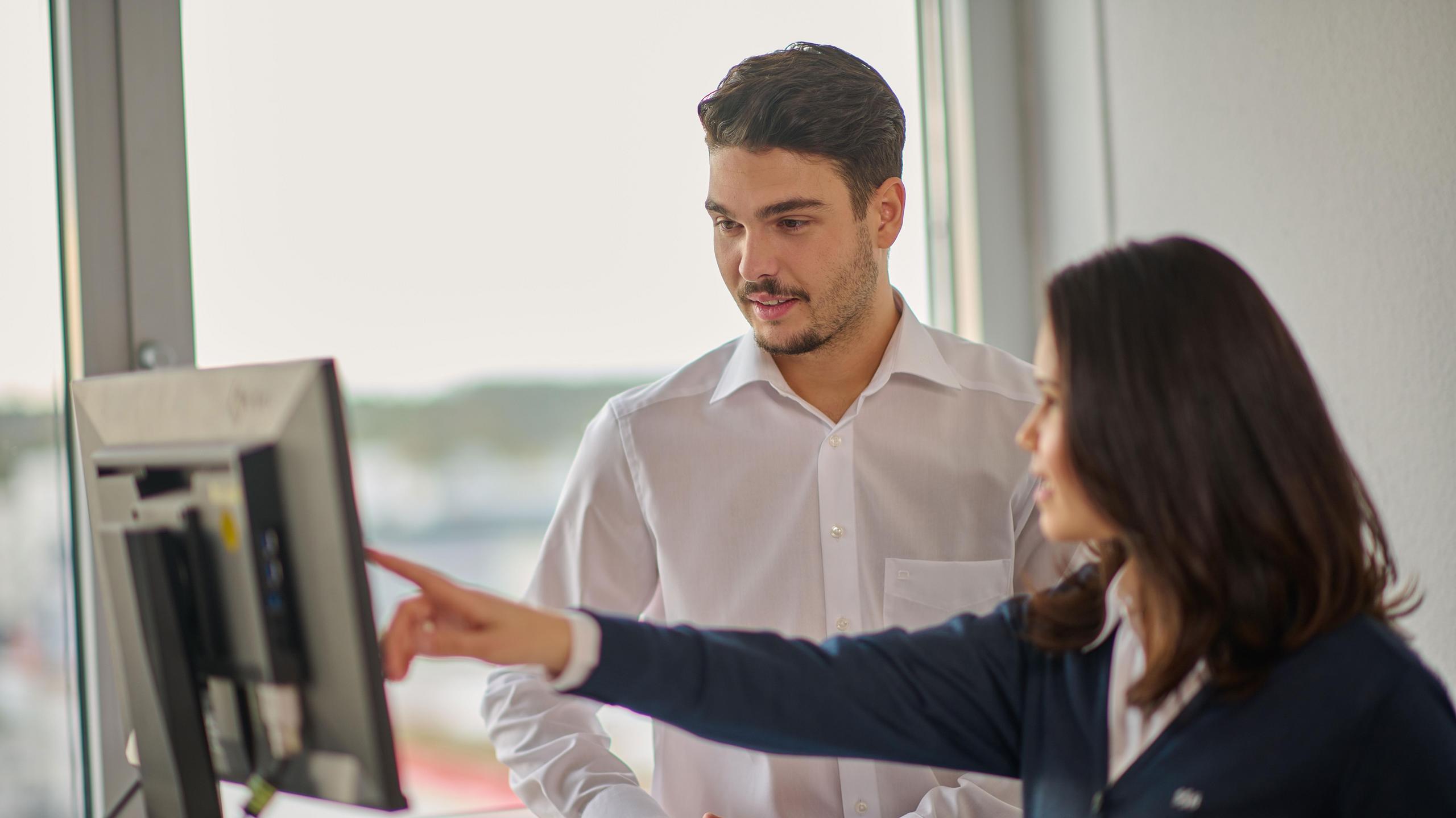 Eine Mitarbeiterin in SSB-Fahrerkleidung zeigt einem jungen Auszubildenden etwas auf einem PC-Bildschirm.
