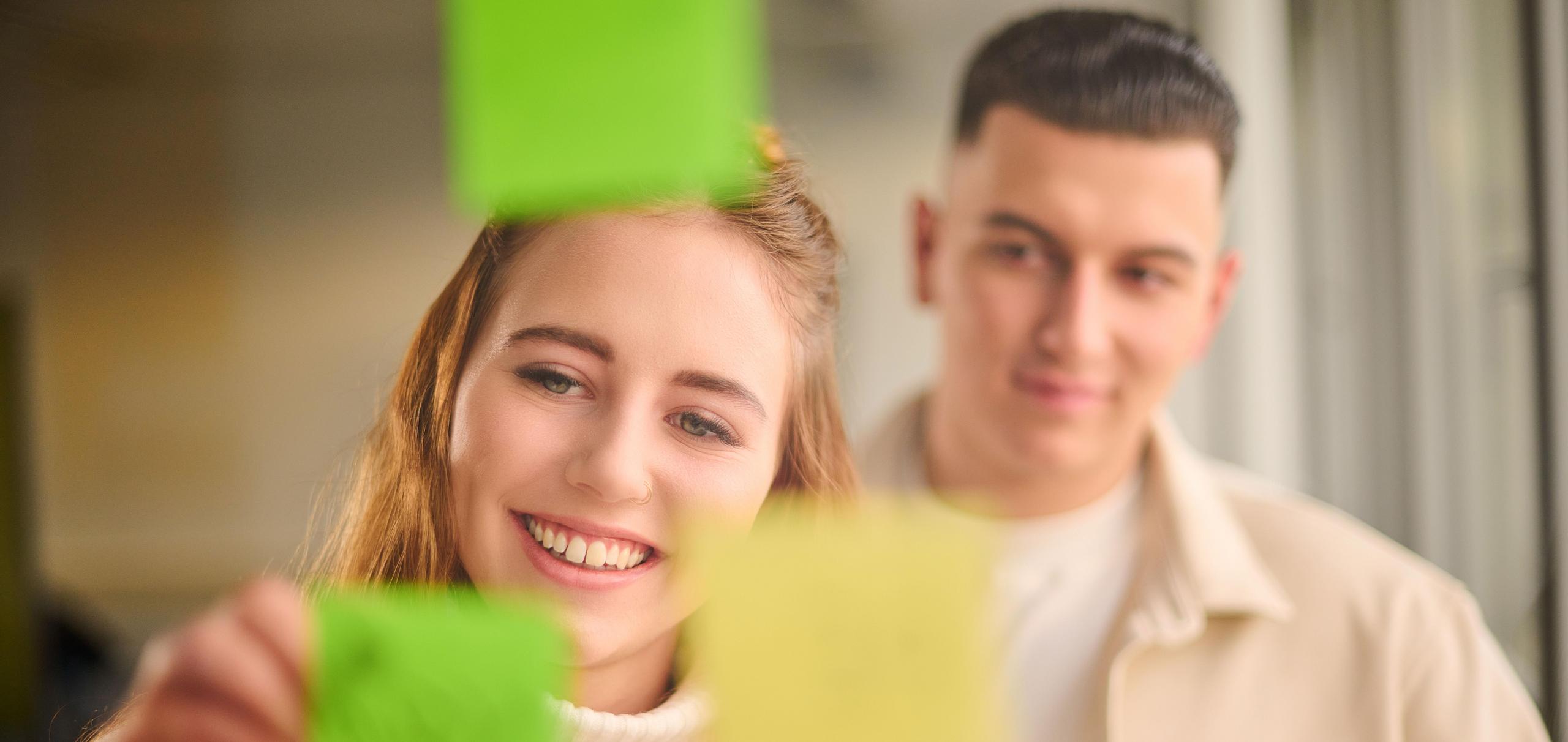 Zwei Auszubildende beschriften einen Notizzettel.