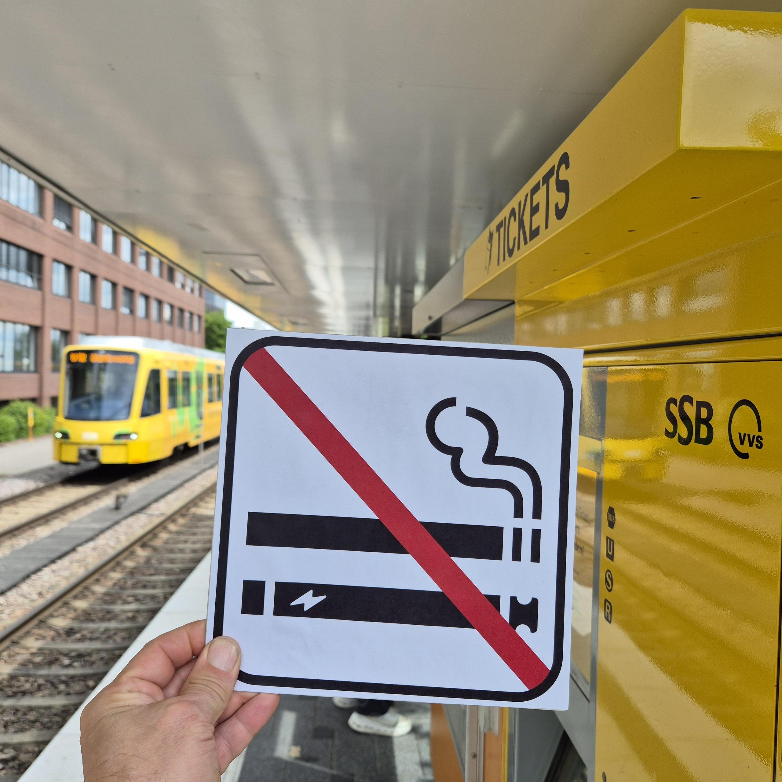 Eine Hand hält das Zeichen für Rauchverbot - zwei durchgestrichene Zigaretten - an einer SSB-Haltestelle in die Luft. 