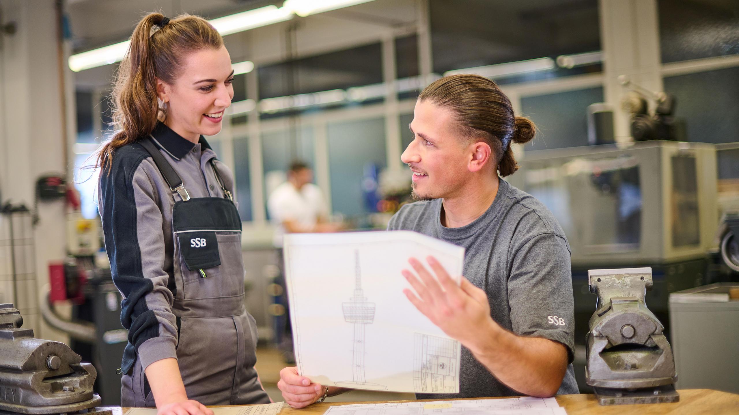 Ein Werkstattmeister unterhält sich mit einer Auszubildenden in der Lehrwerkstatt.