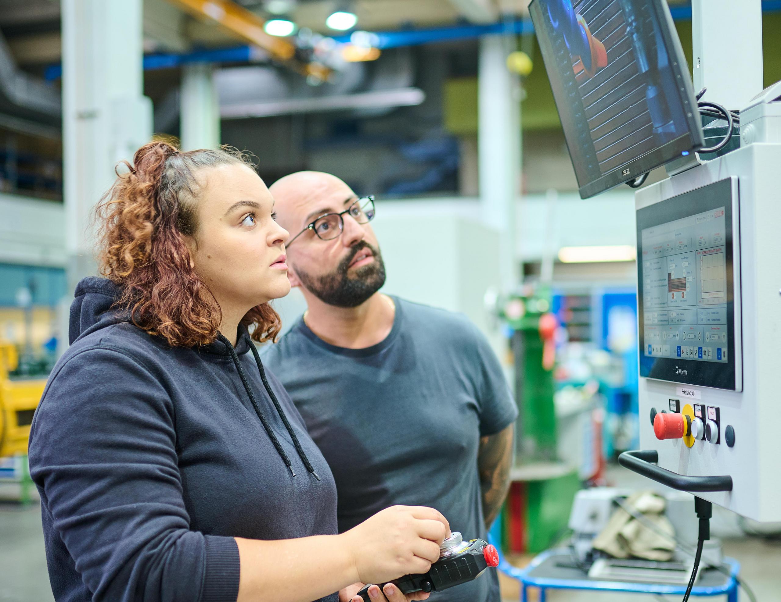 Eine Mitarbeiter und ein Mitarbeiter aus der technischen Werkstatt kontrollieren Werte auf einen Prüfmonitor.