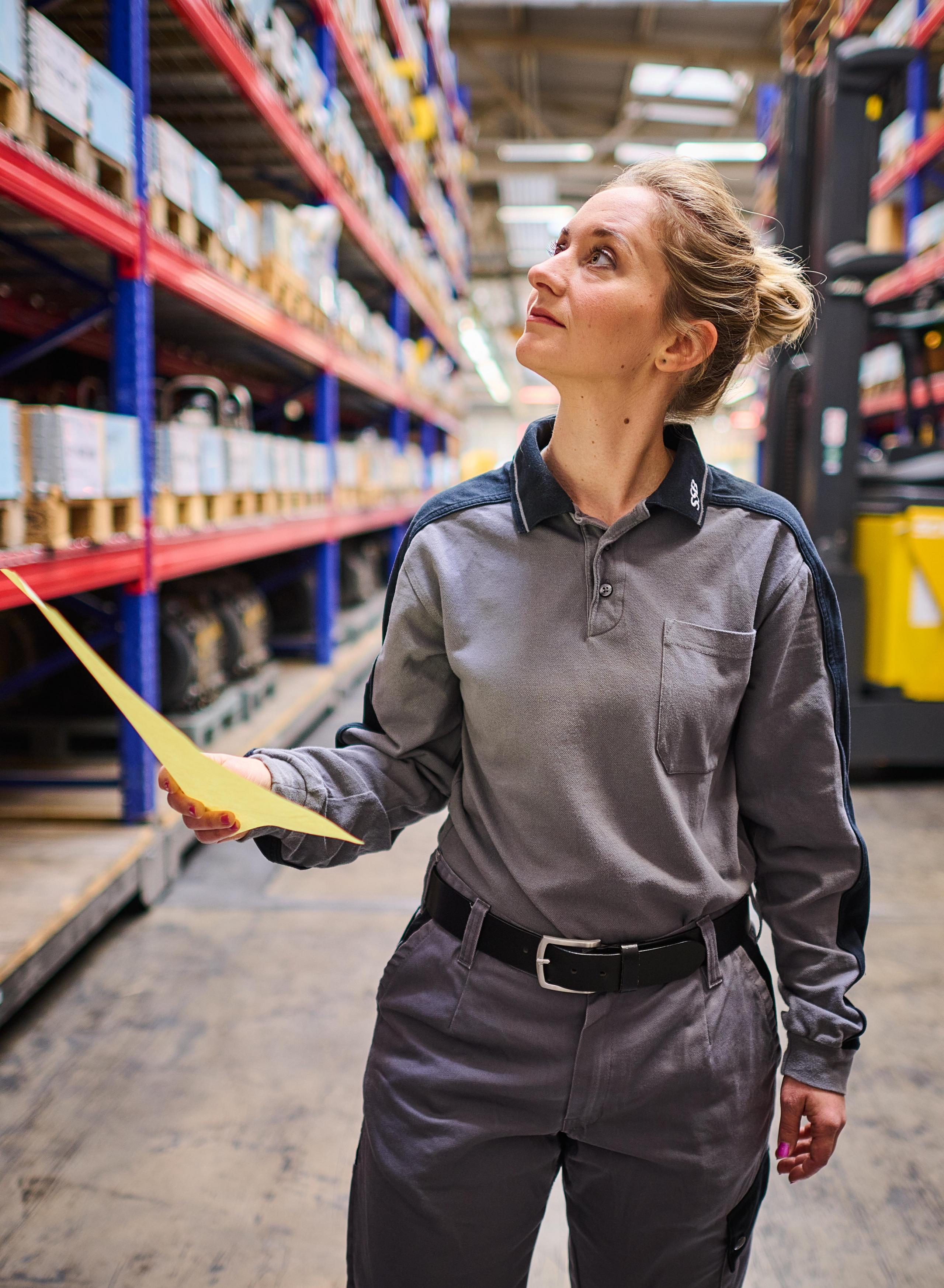 Eine Logistikerin schaut nach oben in ein Regal.