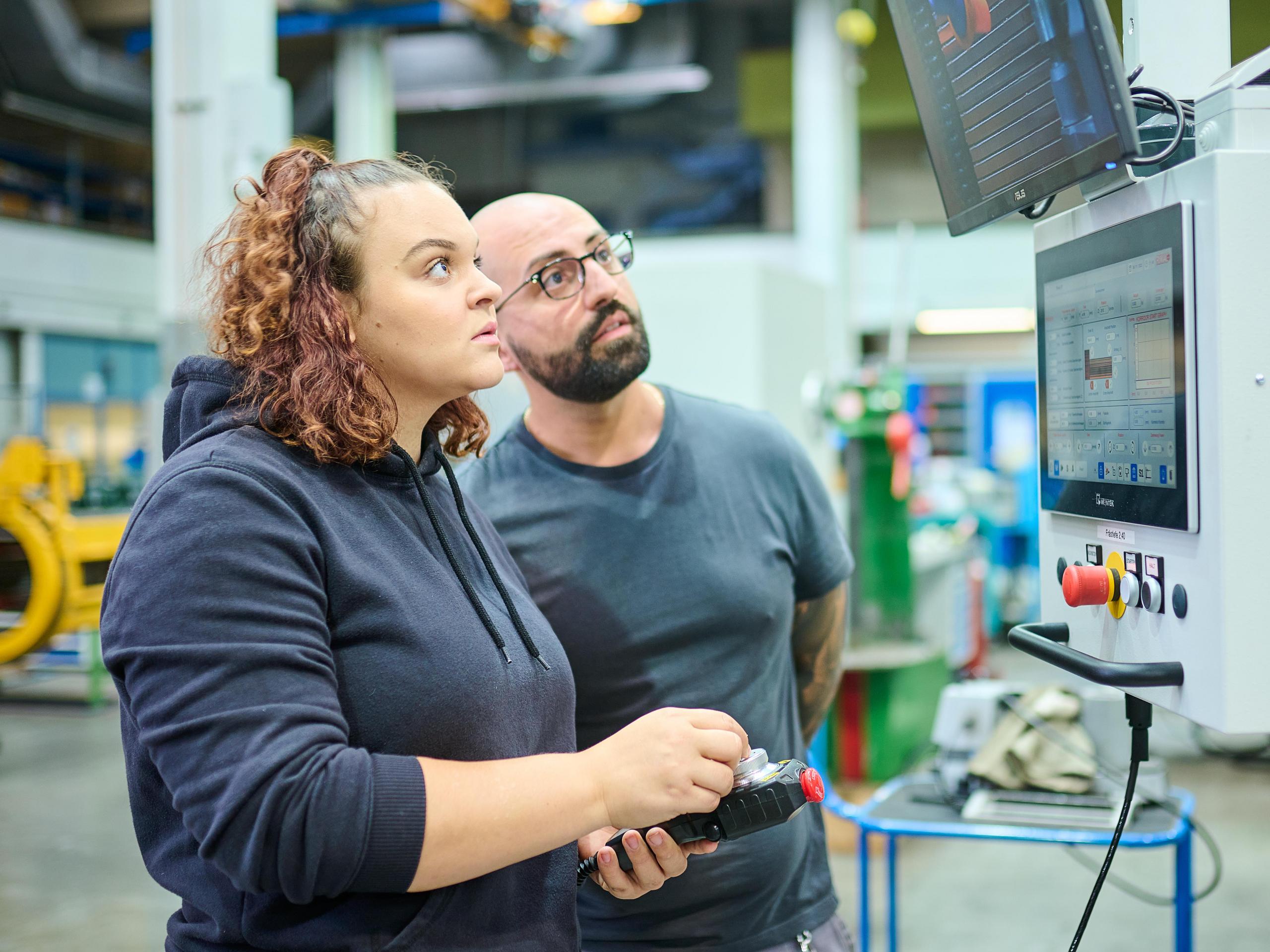 Eine Mitarbeiter und ein Mitarbeiter aus der technischen Werkstatt kontrollieren Werte auf einen Prüfmonitor.