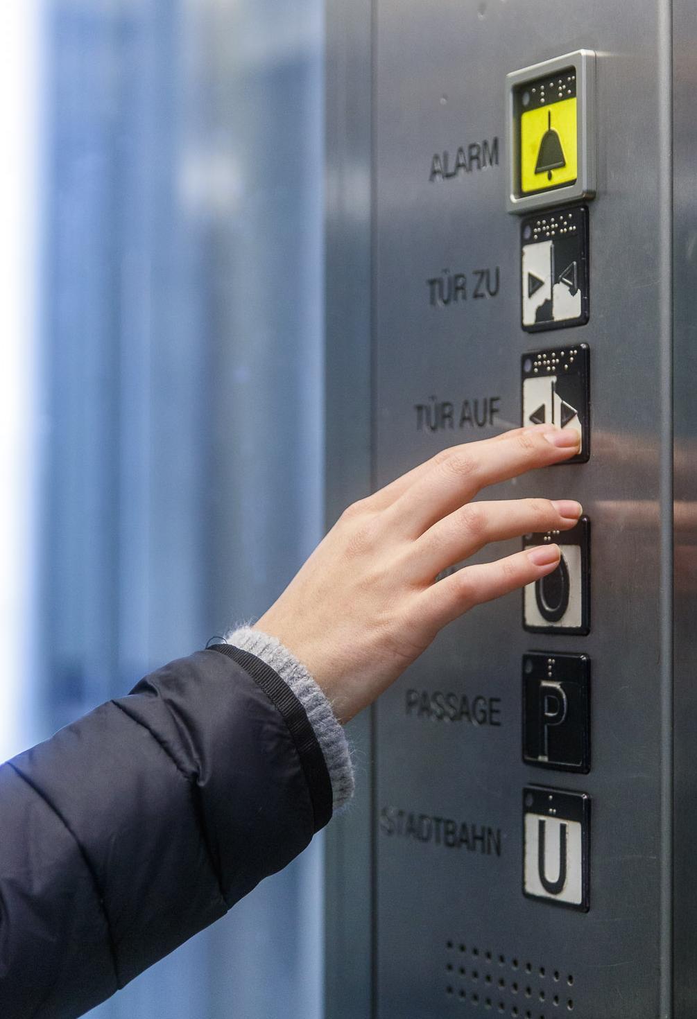 Person bedient einen Knopf im Aufzug