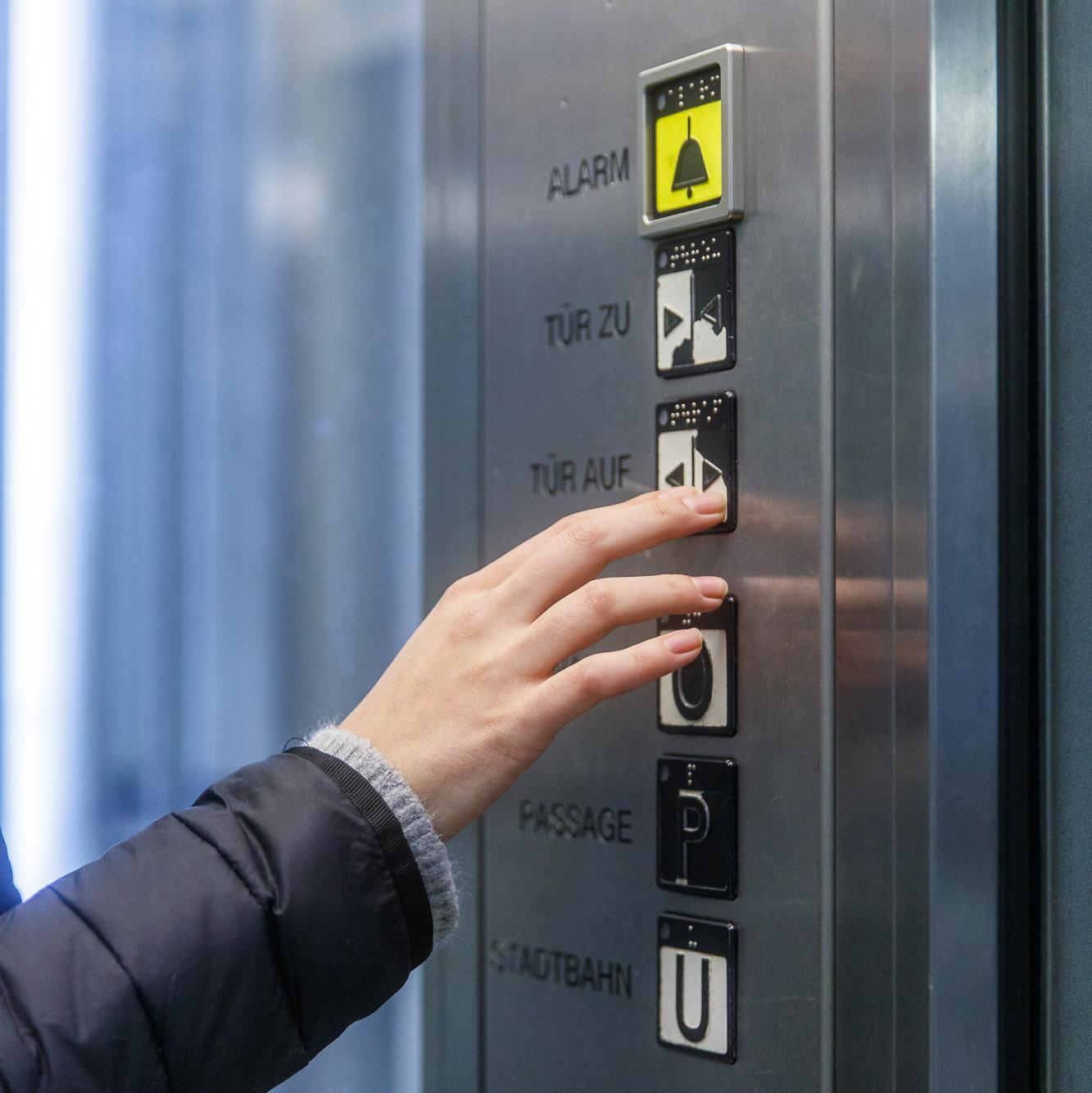 Person bedient einen Knopf im Aufzug