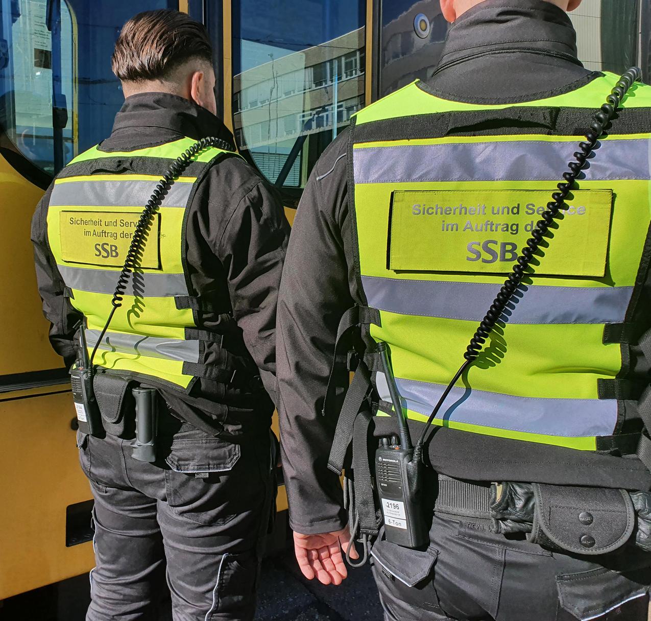 Sicherheitspersonal mit gelben Warnjacken neben einer Stadtbahn