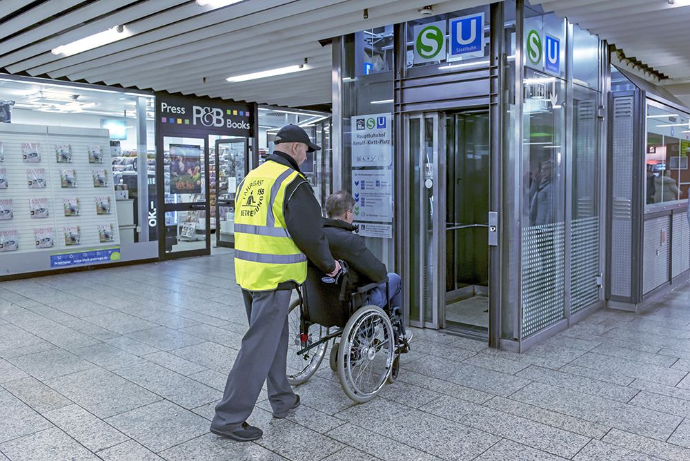 Fahrgastbetreuer hilft Rollstuhlfahrer in einen Aufzug