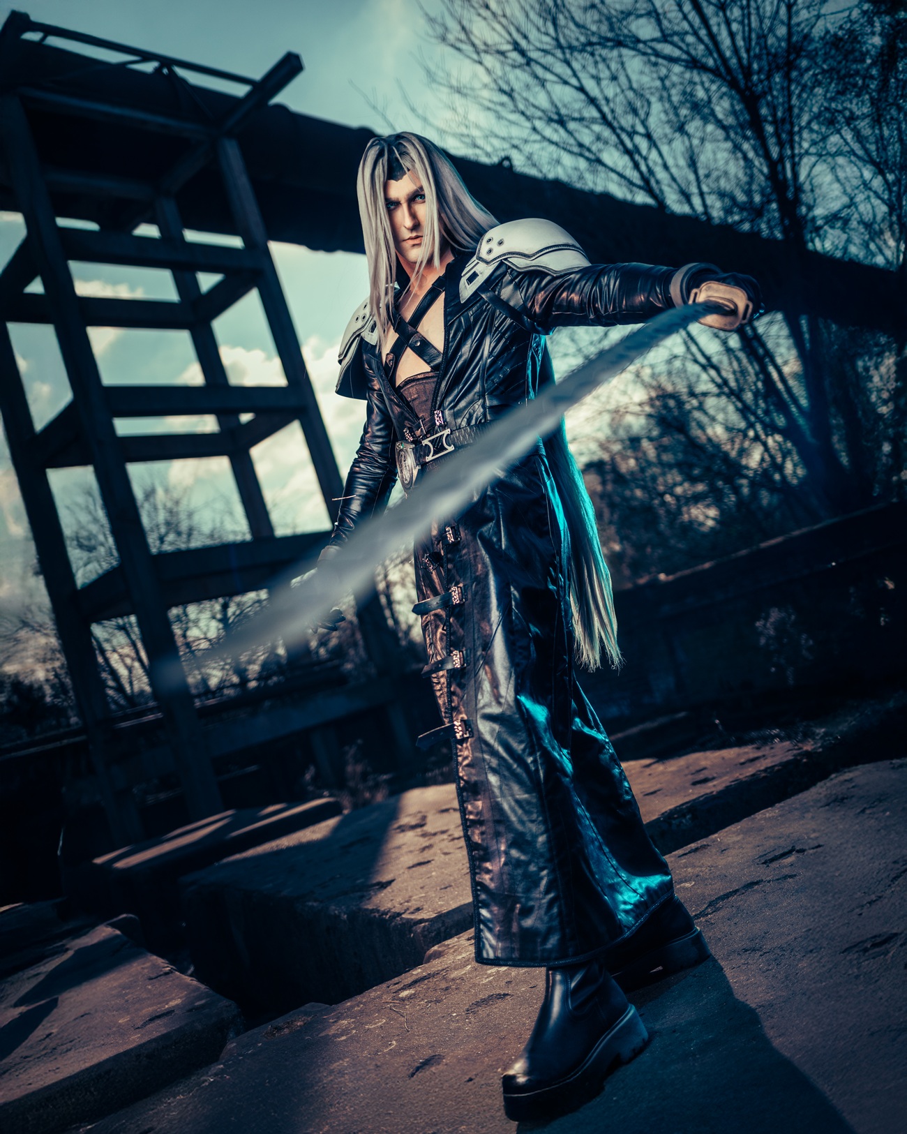 Cosplayer in einem schwarzen Fantasy-Kostüm mit silbernen Schulterpanzern und langem Schwert auf einem industriellen Außengelände.