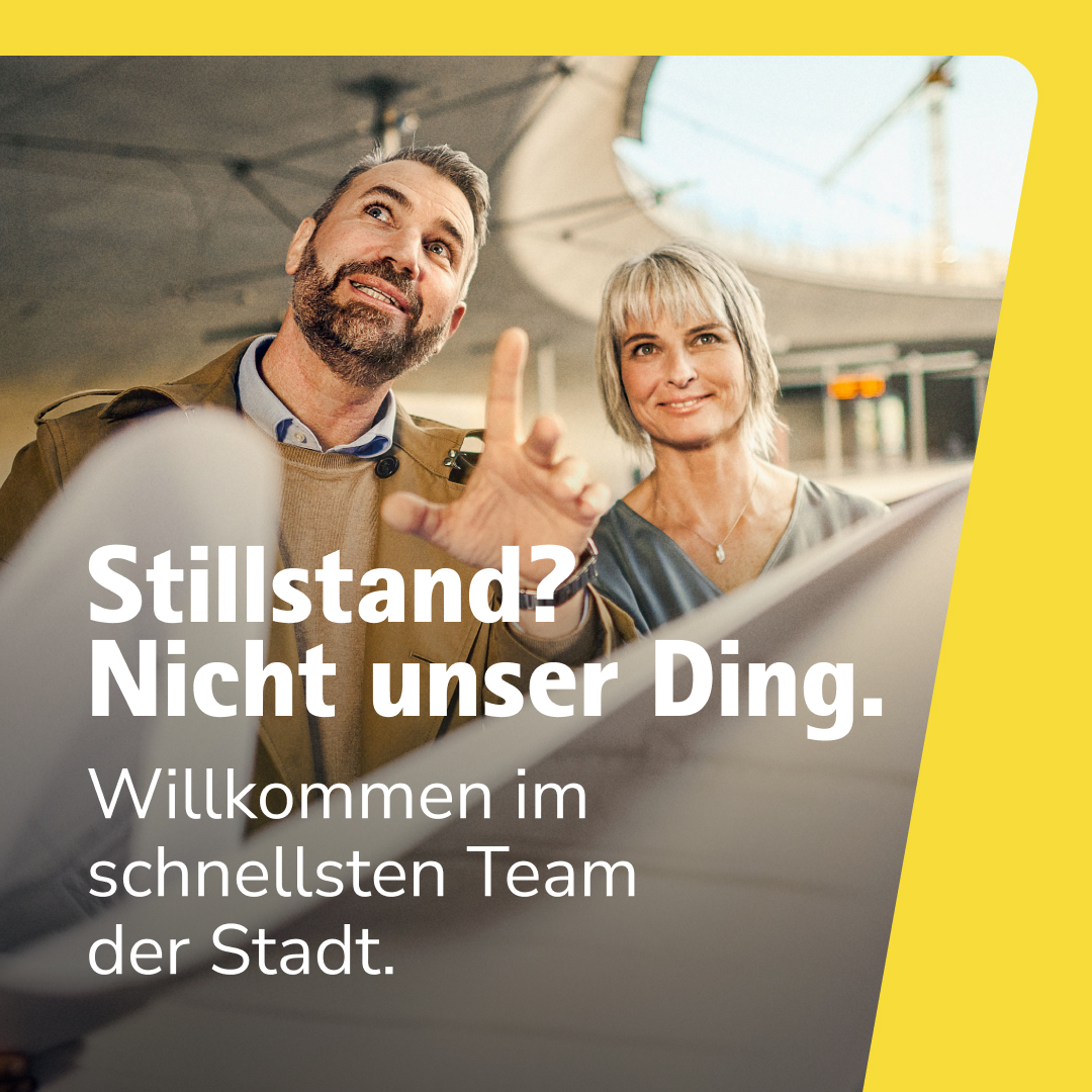 Image-Kampagne Stillstand Eine Frau und ein Mann mittleren Alters stehen an einer Haltestelle.