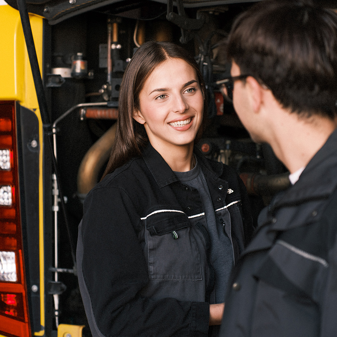 Zwei junge Auszubildende stehen vor dem Busmotor.